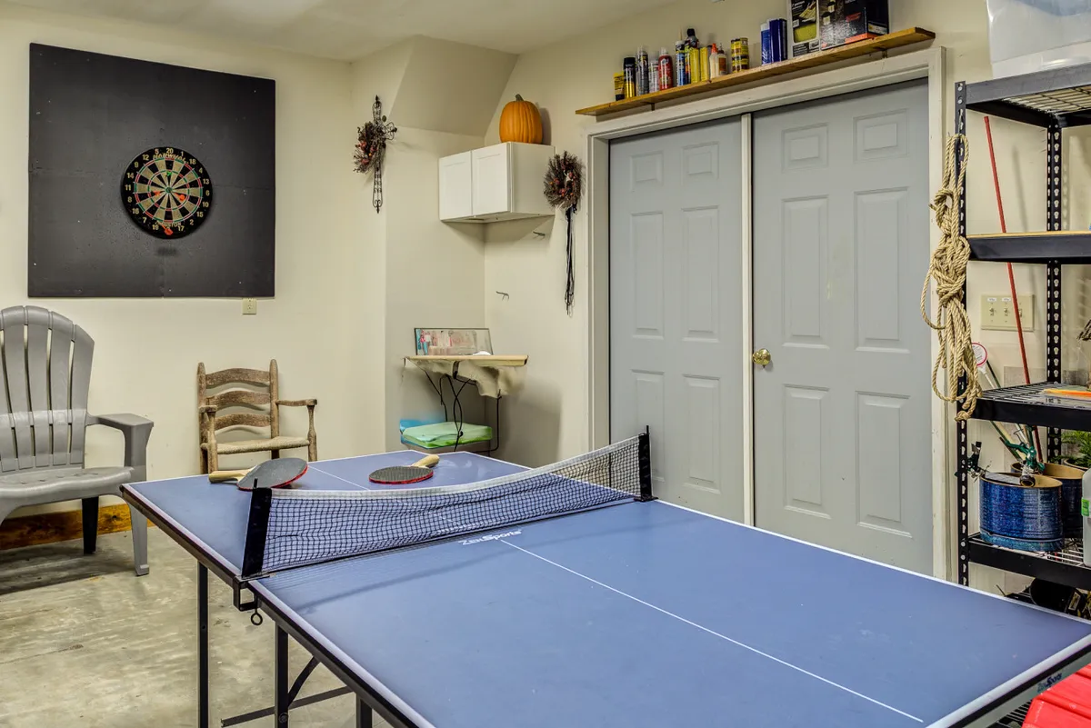 A spacious bonus room filled with a ping pong table and a dartboard mounted on the wall. The seating area and festive pumpkin decor highlight the room's versatility for game nights and celebrations, creating an easygoing, festive environment.