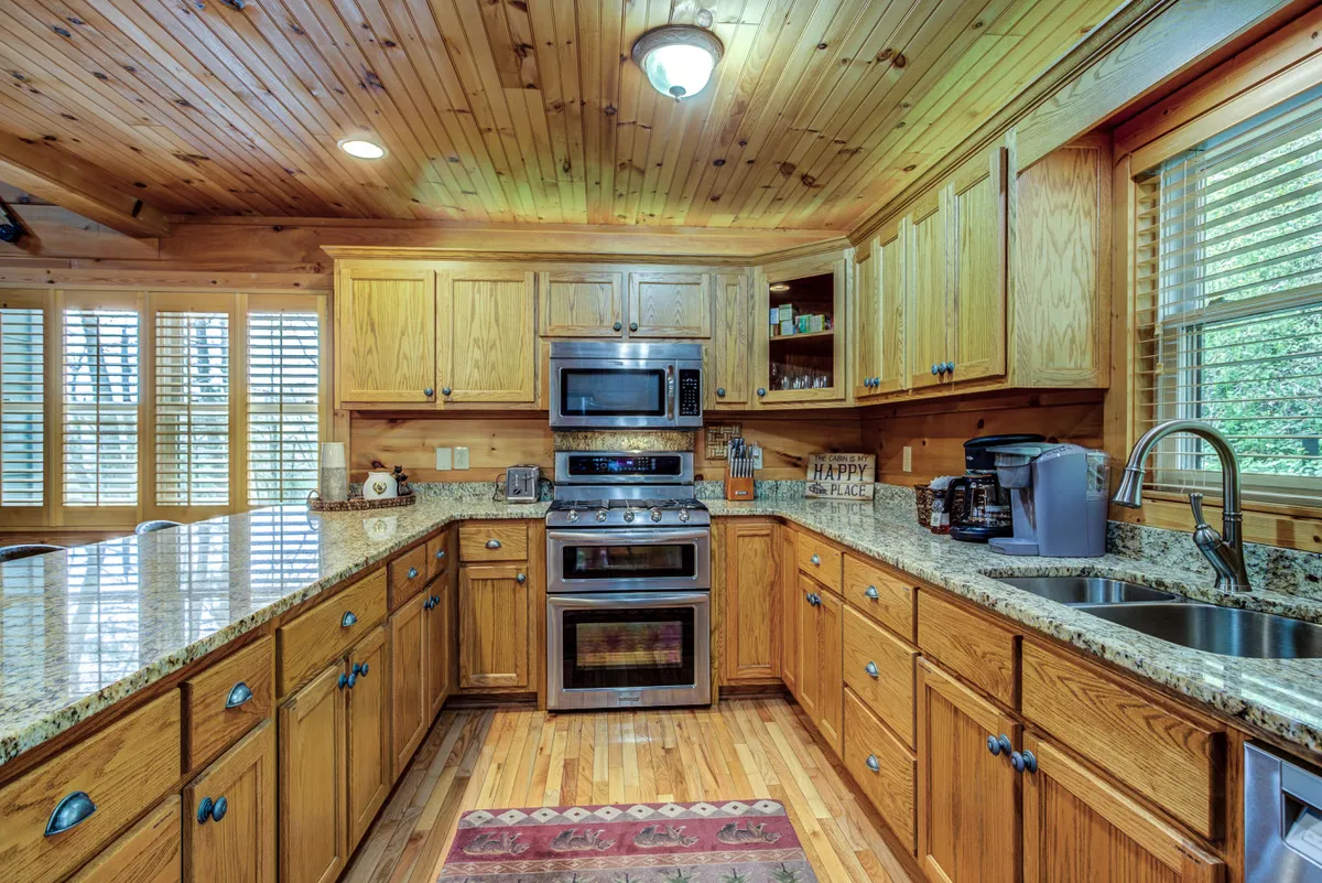 This image spotlights the kitchen with its granite countertops, stainless steel appliances, warm wooden cabinetry, and stylish rug. The breakfast bar is also visible, inviting casual meals or coffee chats.