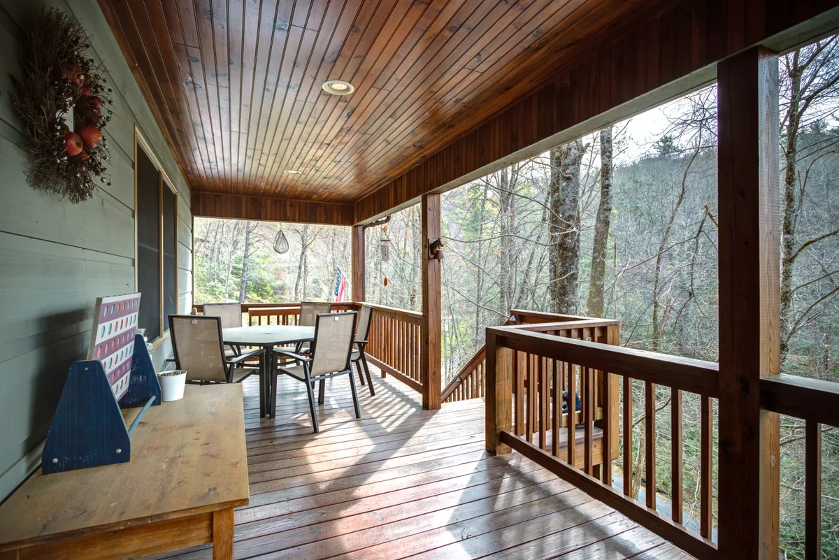 This image features a wooden deck with an outdoor dining table set amid tall trees. The setting is perfect for alfresco meals, morning coffee, or simply enjoying the tranquil forest atmosphere. The space feels welcoming for both people and their pets.