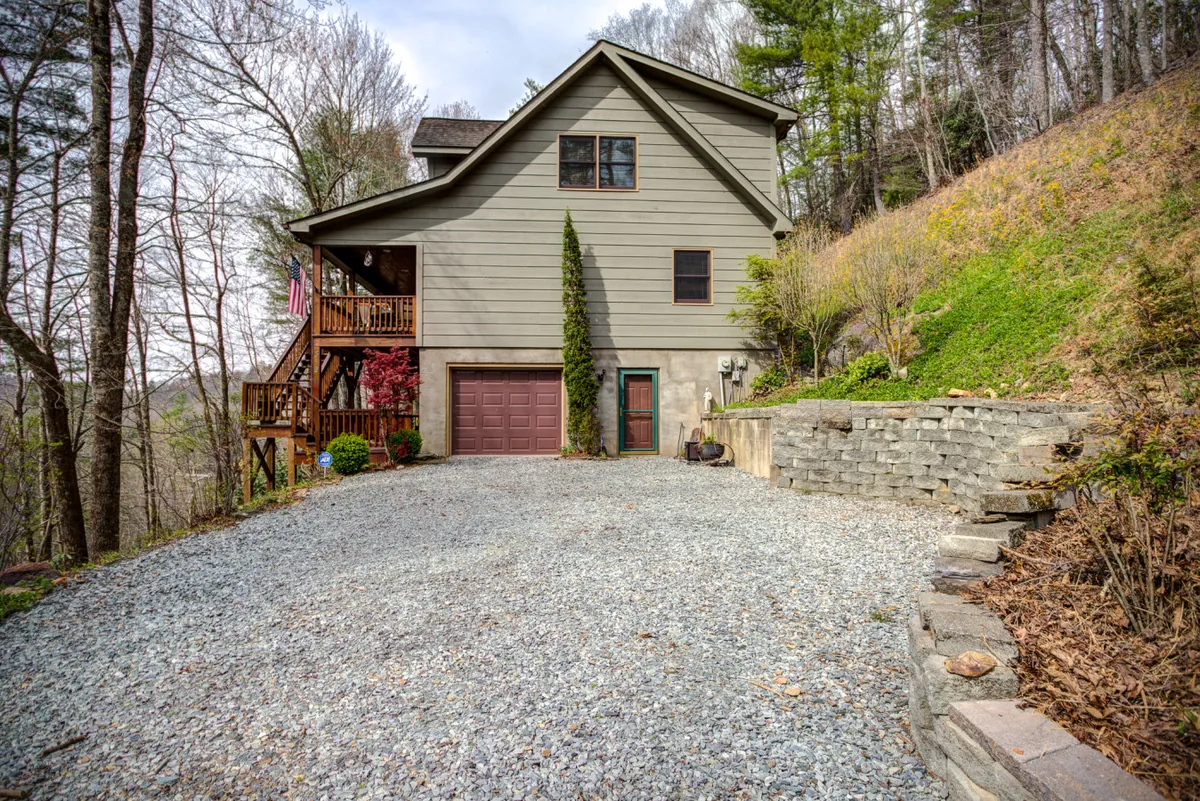 The cabin is shown with its gravel driveway and surrounded by mature trees, emphasizing its peaceful mountain setting. The broad view highlights space for outdoor activities and the connection to the natural landscape, perfect for family gatherings or launching nearby hikes.