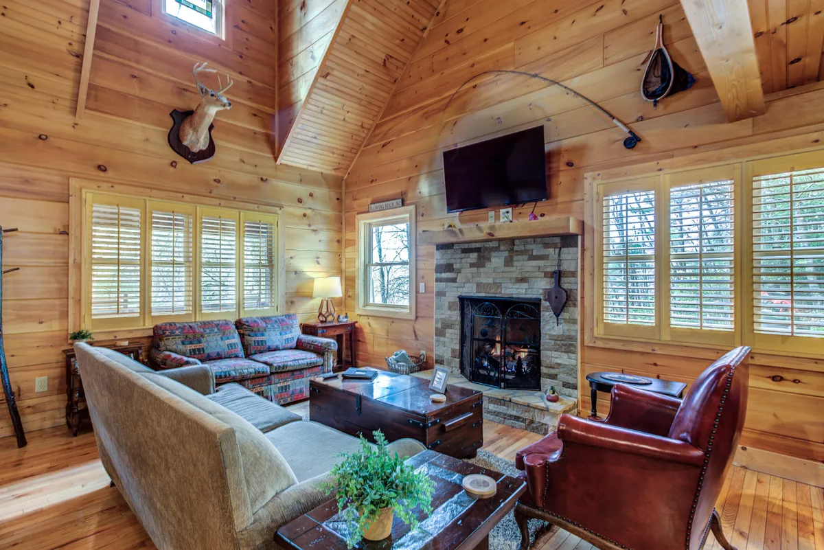 A spacious interior with a comfortable sofa set near a fireplace, wood paneling, and large windows that likely frame views of the snowy woods outside. The scene suggests quiet moments of relaxation and socializing in a warm, inviting setting.
