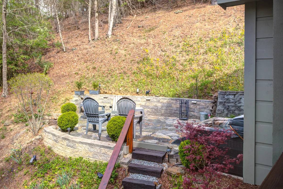 An inviting stone patio set with Adirondack chairs overlooks a lush landscape, likely dusted with snow in winter. The space is open to nature and would easily be transformed into a snowy retreat after a day on the slopes, perfect for gathering around a fire pit or relaxing in the crisp mountain air.