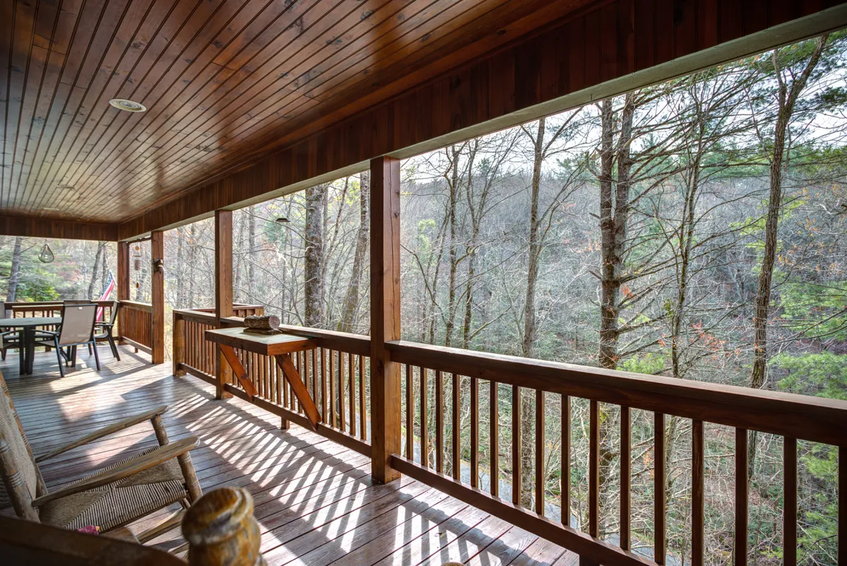 A spacious wooden deck surrounded by tall trees, featuring a dining table perfect for meals or relaxing outdoors. The deck offers a tranquil atmosphere with views of the natural landscape, creating a seamless transition between the comfort of the home and the beauty of the outdoors.