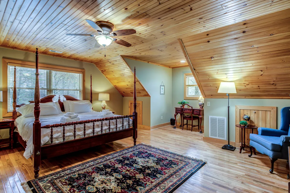 A charming loft space featuring a four-poster bed, a decorative rug, a wooden ceiling, and a reading chair. The area feels playful yet restful, suitable for children or extra guests.