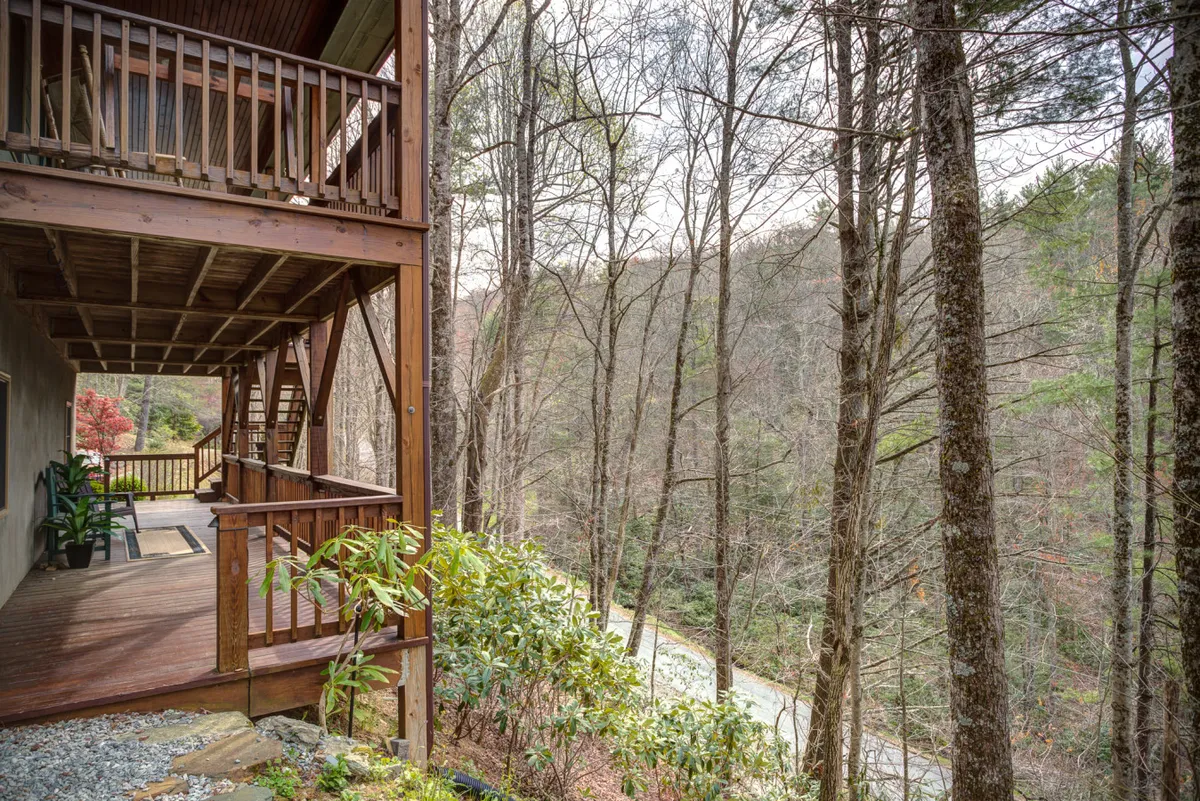 A spacious wooden deck stretches out over the landscape, bordered by trees and overlooking a scenic river. The setting is tranquil, offering space for relaxation or playful moments with a pet after a walk.