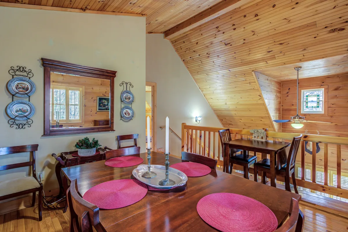 The wooden dining table is set with decorative plates, candles, and pink placemats, creating a cozy, festive environment. The reflection in the wall mirror and surrounding decor suggest space for both intimate and larger gatherings.