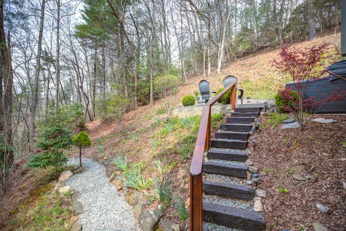 Stone steps lead to a cozy arrangement of Adirondack chairs set among landscaped greenery and mature trees. The scene evokes relaxation and connection with nature, ideal for watching sunsets, stargazing, or resting after a day’s adventure.