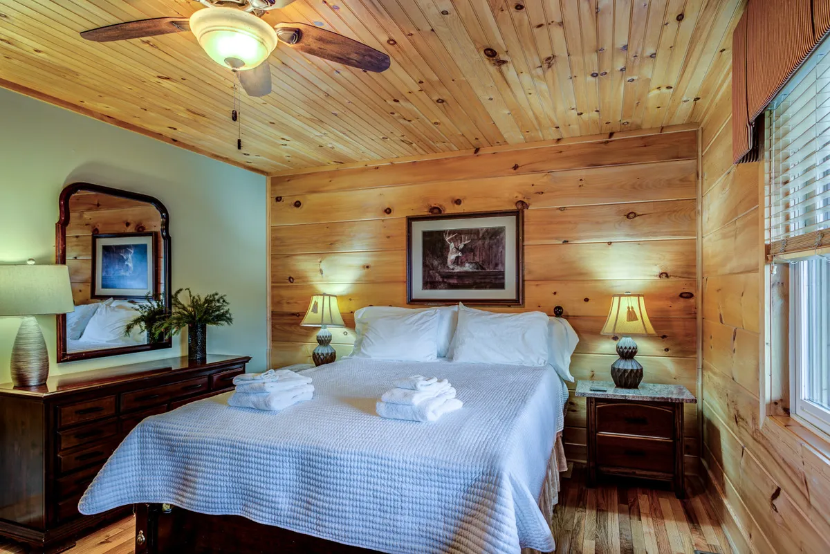 This image features a cozy bedroom with a comfortable bed, nightstands with soft lighting from lamps, a mirror, and tasteful artwork. Natural light filters in, creating a peaceful environment ideal for rest and relaxation.