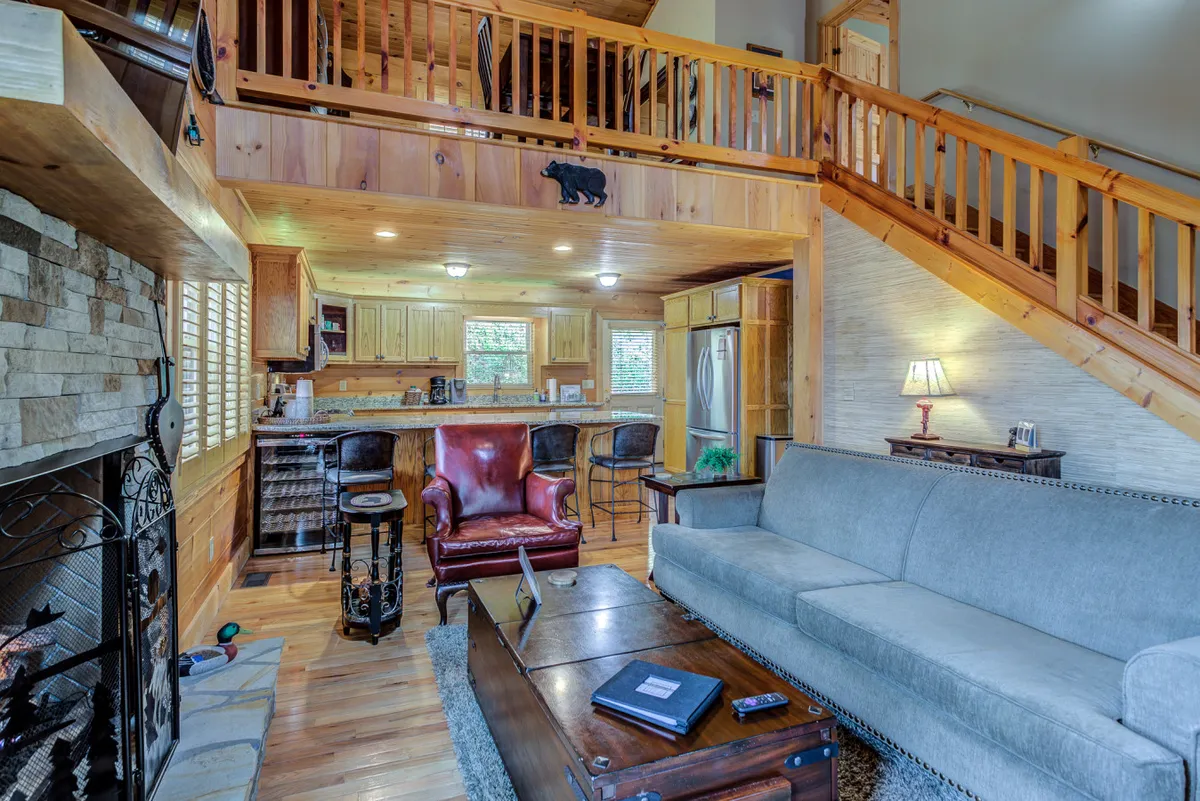 A cozy living area featuring a glowing fireplace, wooden staircase, comfortable seating, and a kitchen bar. The ambiance is warm and inviting, emphasizing a welcoming retreat where guests can unwind after cold winter adventures.