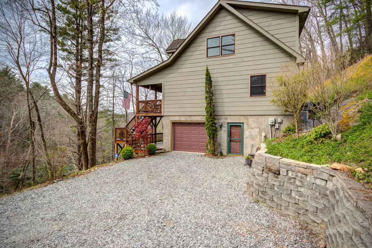 This image features the cabin's exterior, showcasing the house nestled among trees with a view of the driveway and a well-kept garden area. The porch offers a relaxing spot to take in the surrounding nature. The yard provides ample space for children to play and family gatherings.